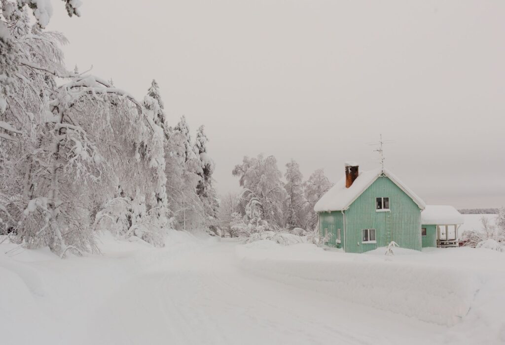 Vanha vaalena vihreä rintamamiestalo lumisessa maisemassa metsätien varrella